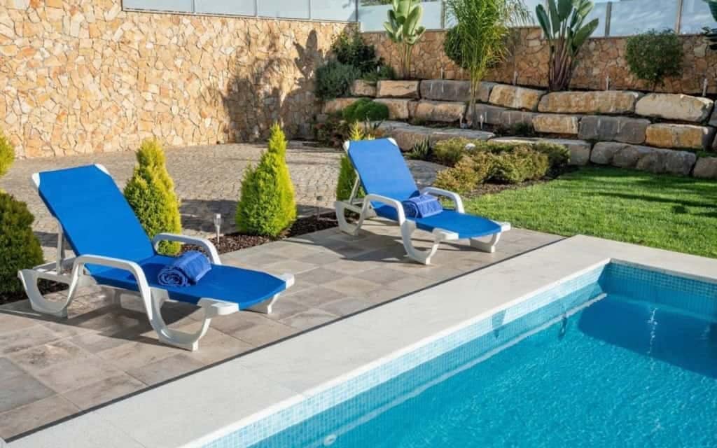 Outdoor swimming pool area with natural stone patio paving, pool coping, and landscaped retaining stone walls