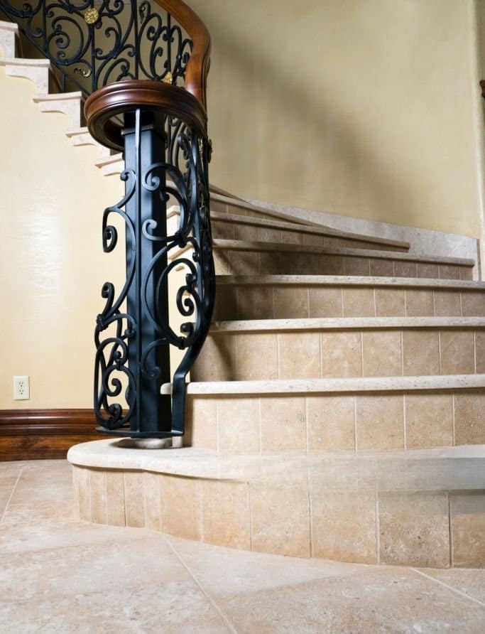 Luxury interior staircase with natural stone treads and decorative wrought iron balustrade