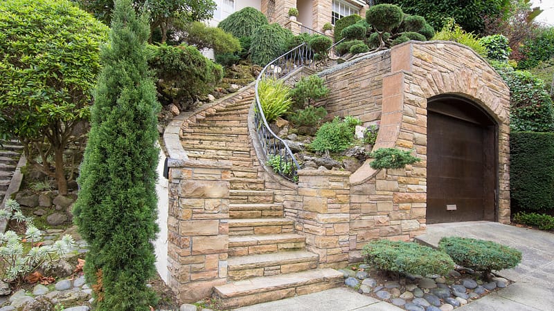 Natural stone veneer exterior with curved staircase, retaining wall, and arched entrance